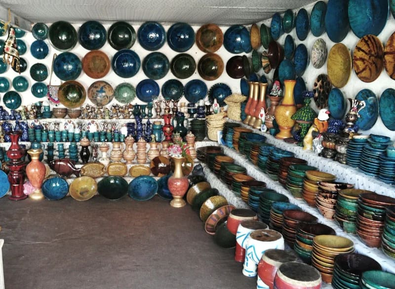 Shelves and walls of a shop crowded with turquoise, green and brown glazed bowls, plates and vases.