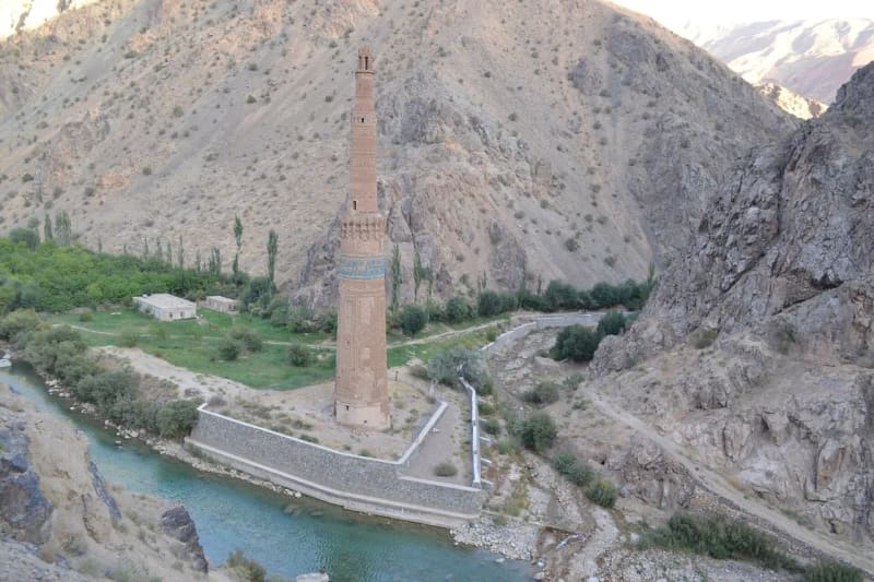 A tall brick minaret on a riverbank at the bottom of a steep rocky gorge.